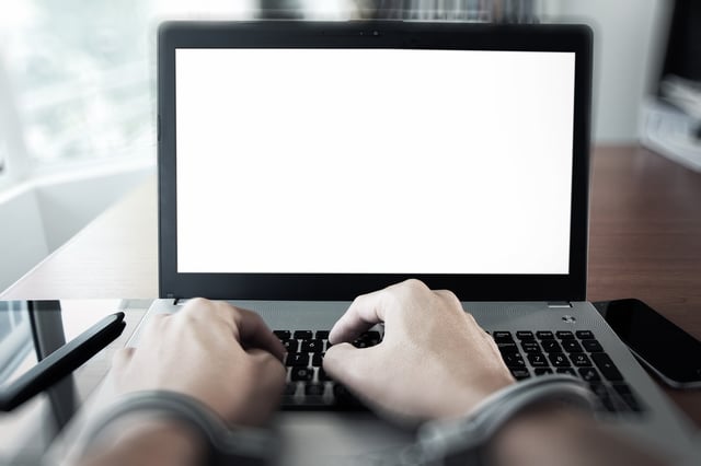 Businessman hand in handcuffs at wooden desk with laptop computer and digital tablet and stylus pen and smart phone as Cyber-Crime concept.jpeg
